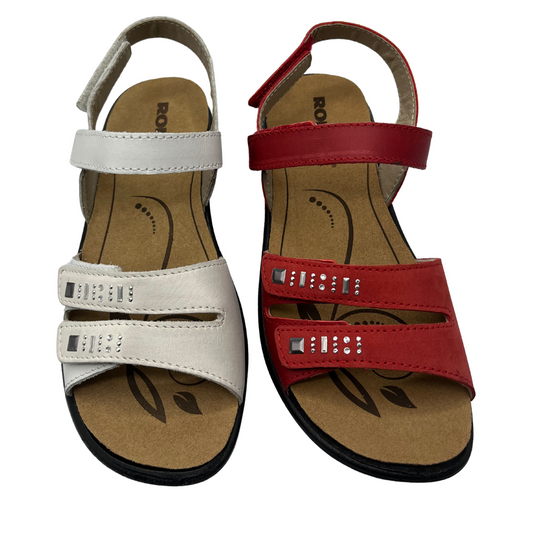 Top view of one white sandal beside one red sandal. Both have double toe straps and two ankle straps