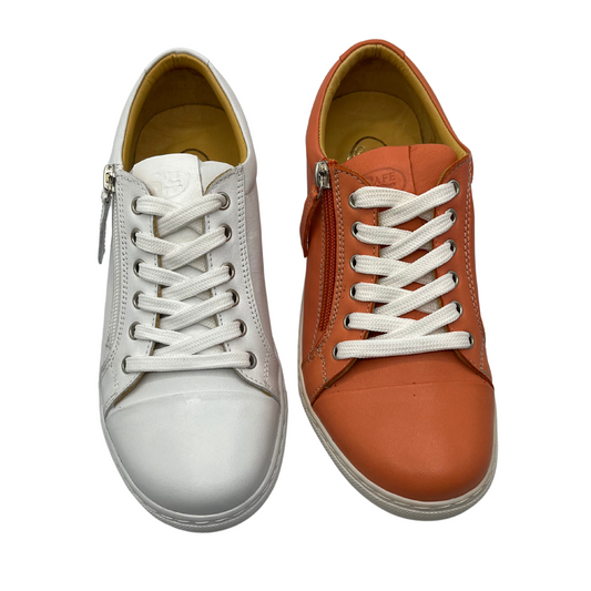 Top view of two sneakers side by side. One is white leather and the other is orange leather. Both have white laces and a side zipper closure.