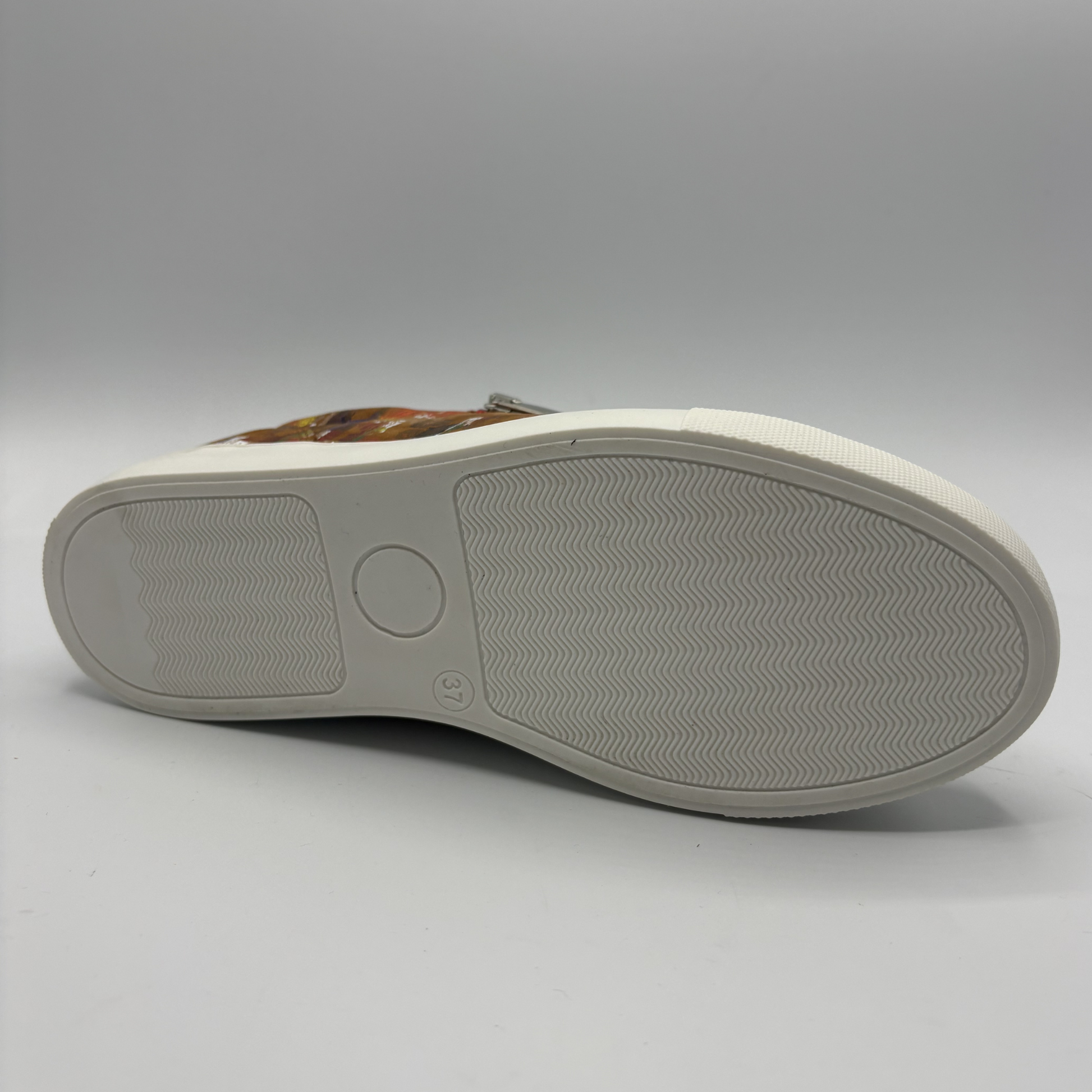 Bottom view of a leather sneaker with a side zip closure and white rubber outsole