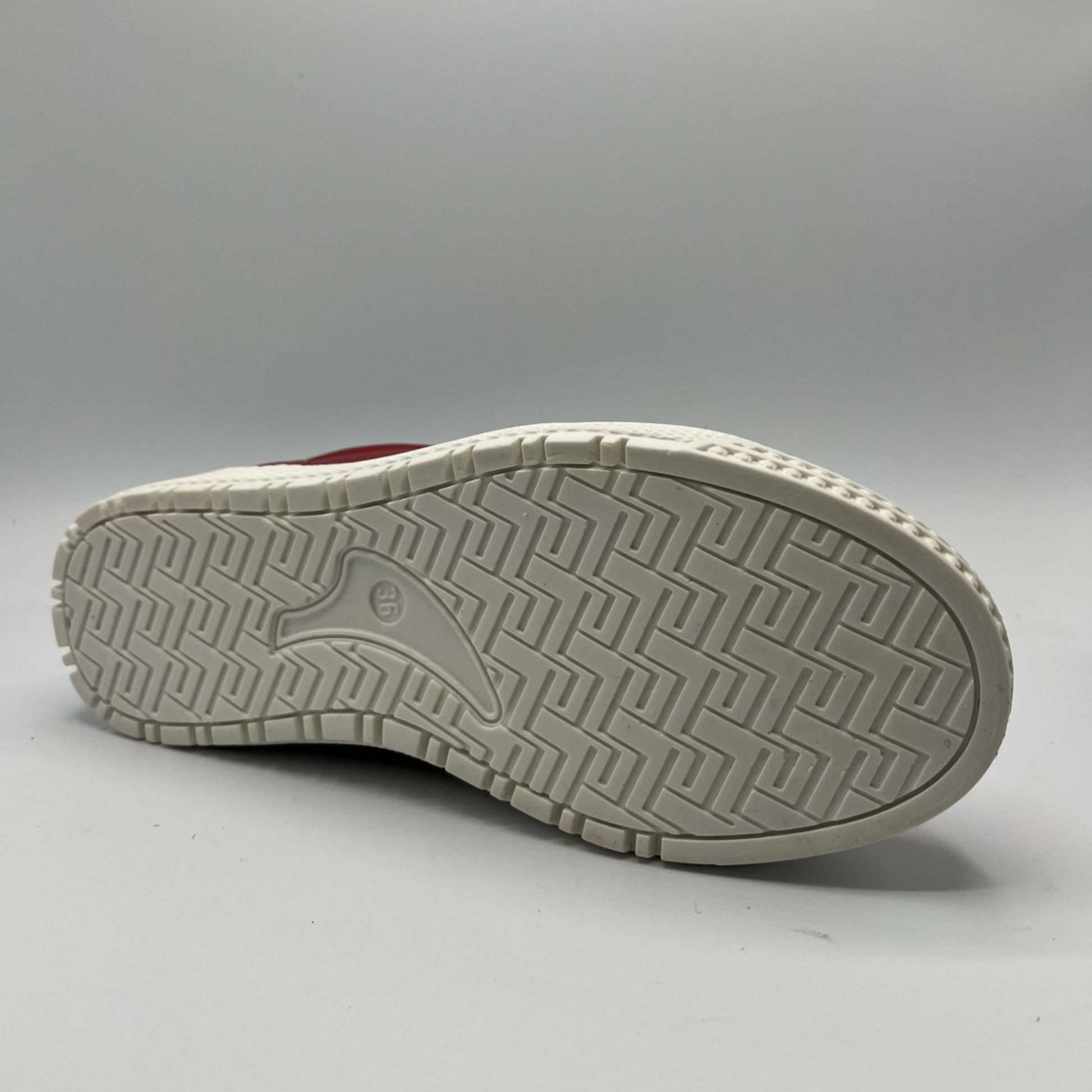 Bottom view of a red leather sneaker with a white rubber outsole.
