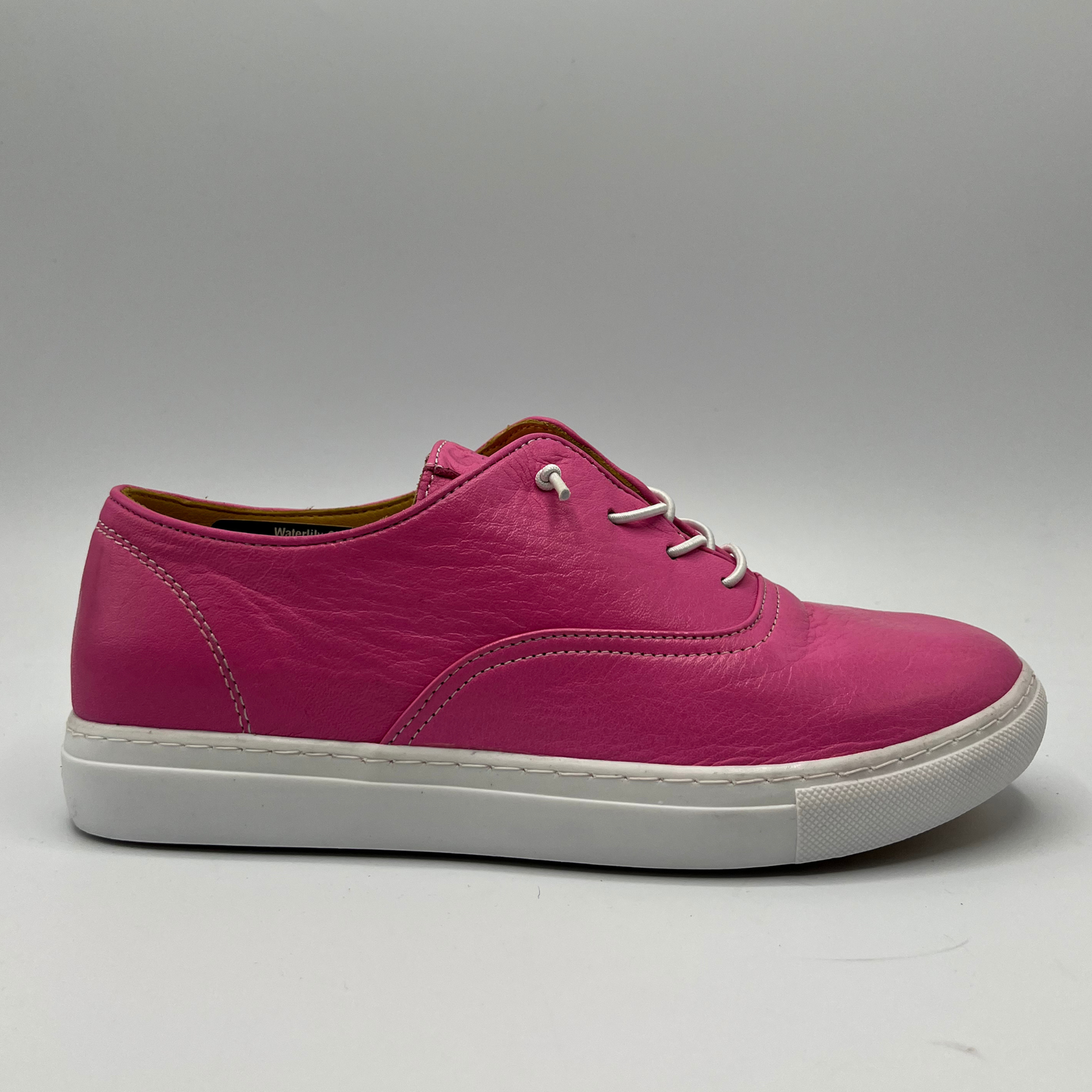 Right facing view of a fuschia leather sneaker with elastic laces and a white rubber outsole.