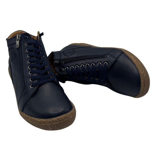 View of a pair of navy leather short boots, one standing up and one laying on its side. Brown rubber outsoles, elastic laces and side zipper closure