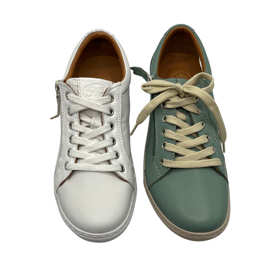 Top view of two leather sneakers beside each other. One is white and one is light green. Both have a leather upper and lining and rounded toe.