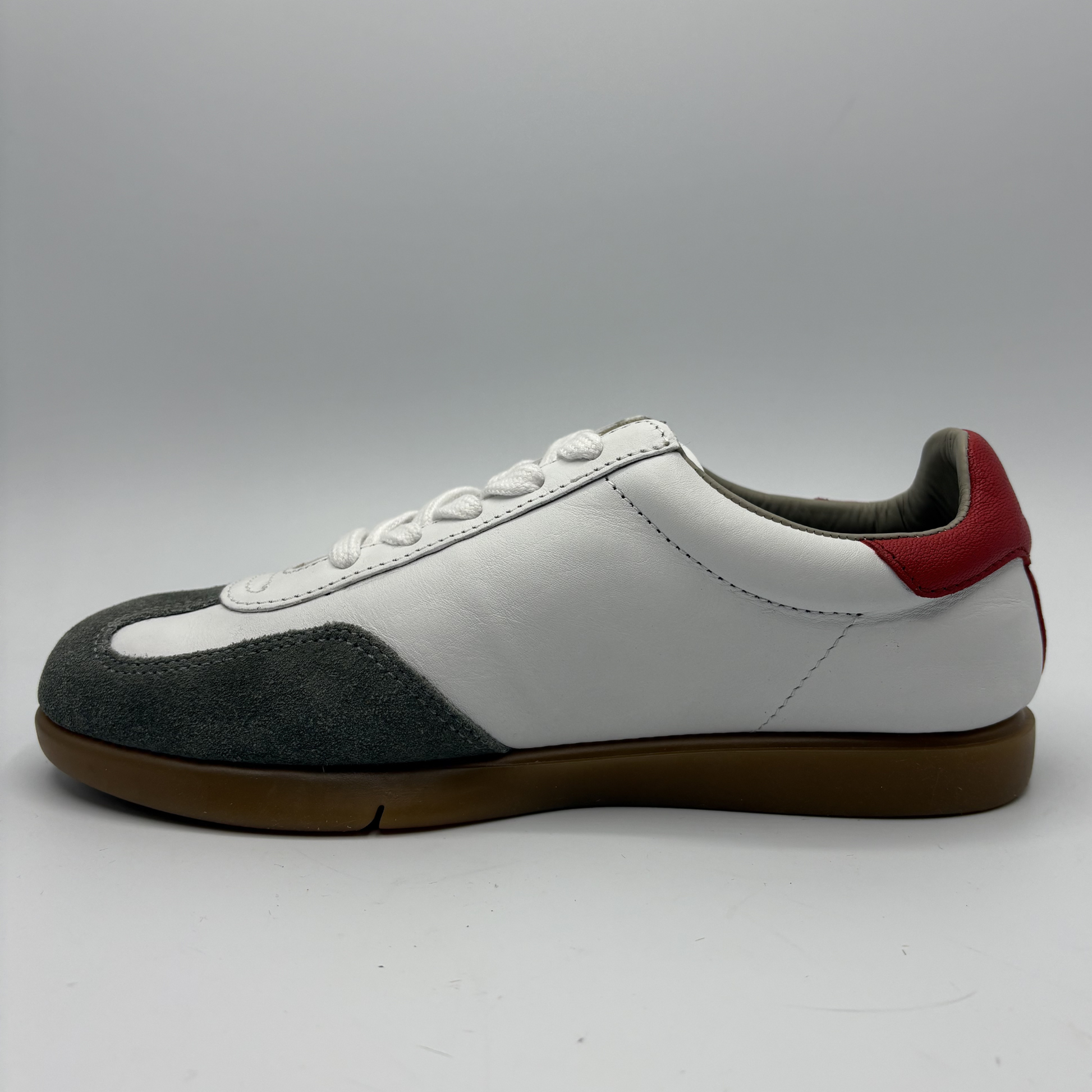 Left facing view of a white sneaker with grey and red accents