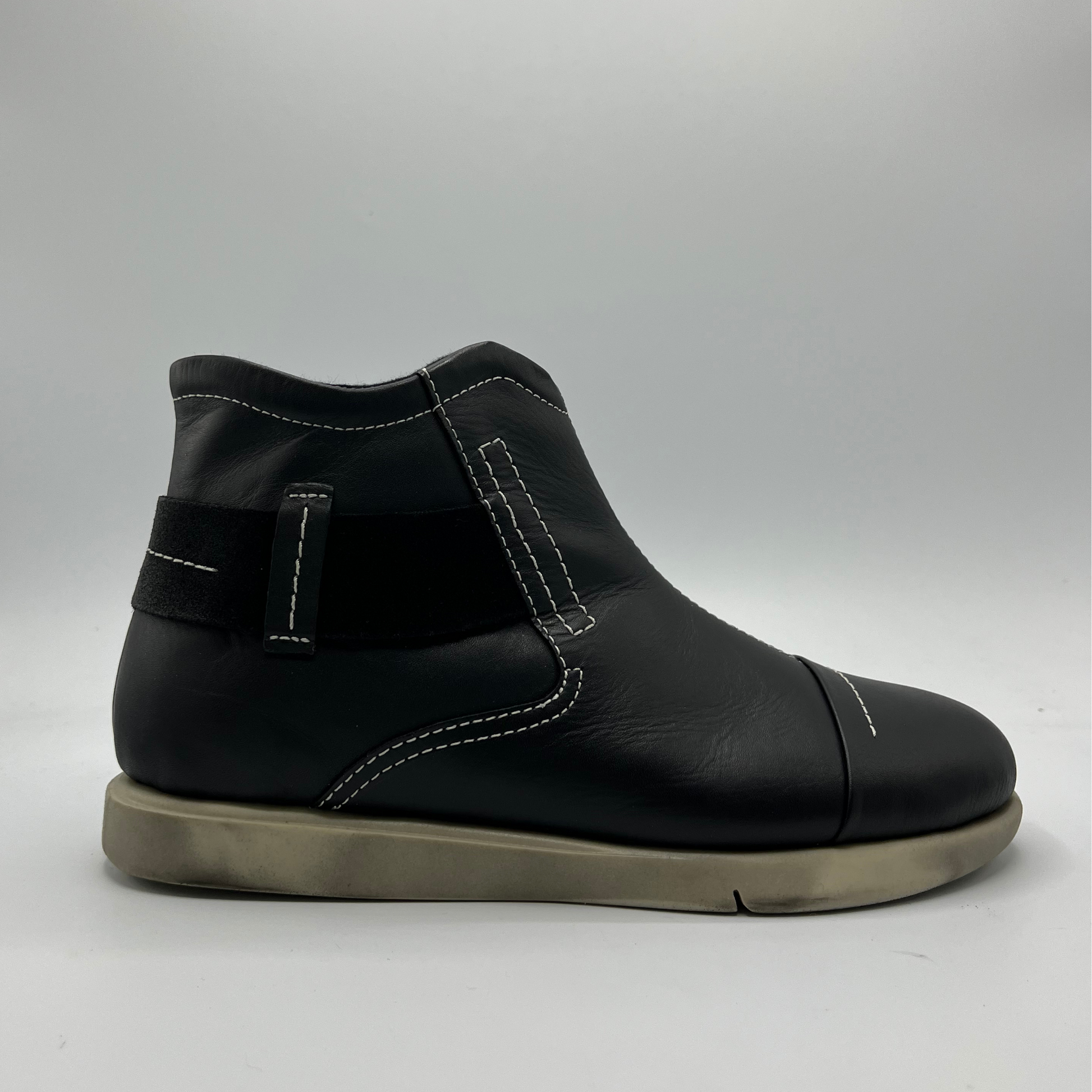 Black leather boot with a strap on a gray background