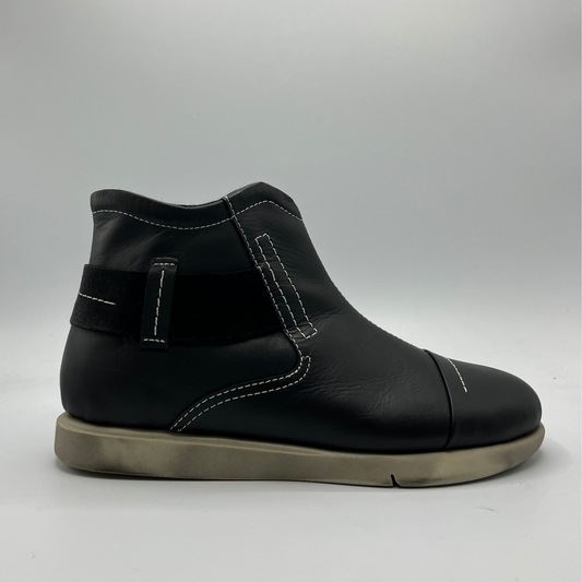 Black leather boot with a strap on a gray background