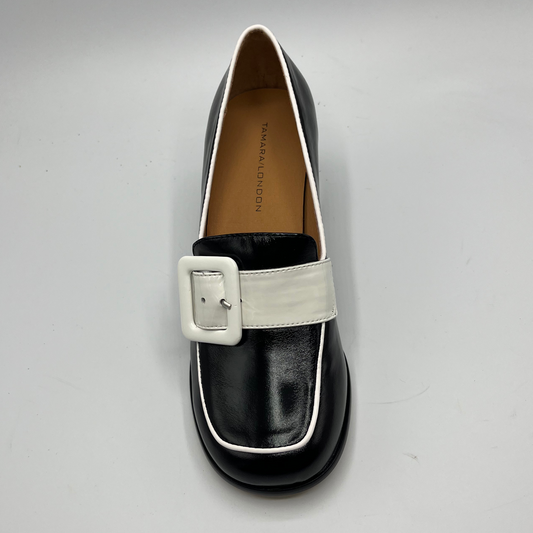 Black loafer with a white buckle on a gray background