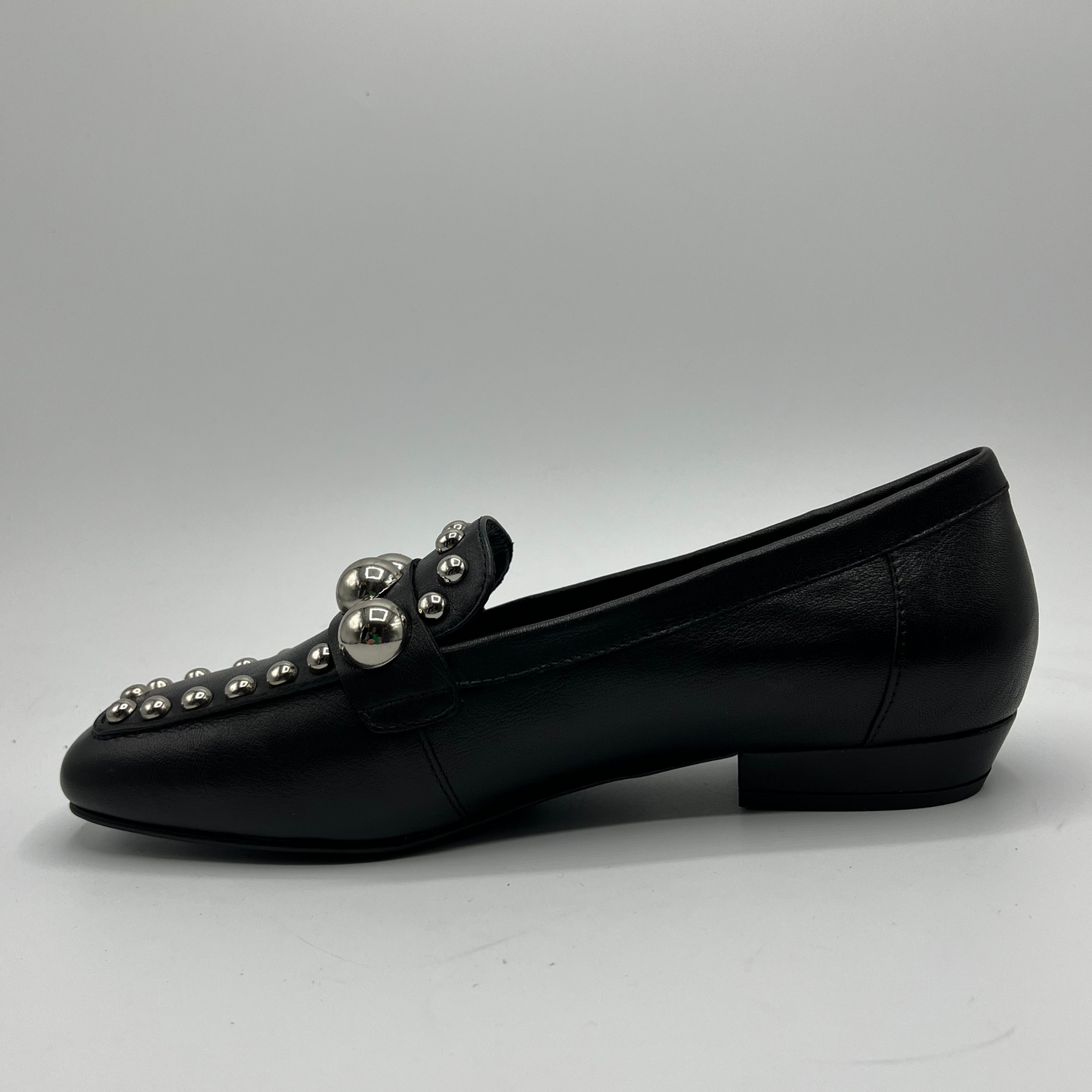 Black loafer shoe with silver embellishments on a gray background