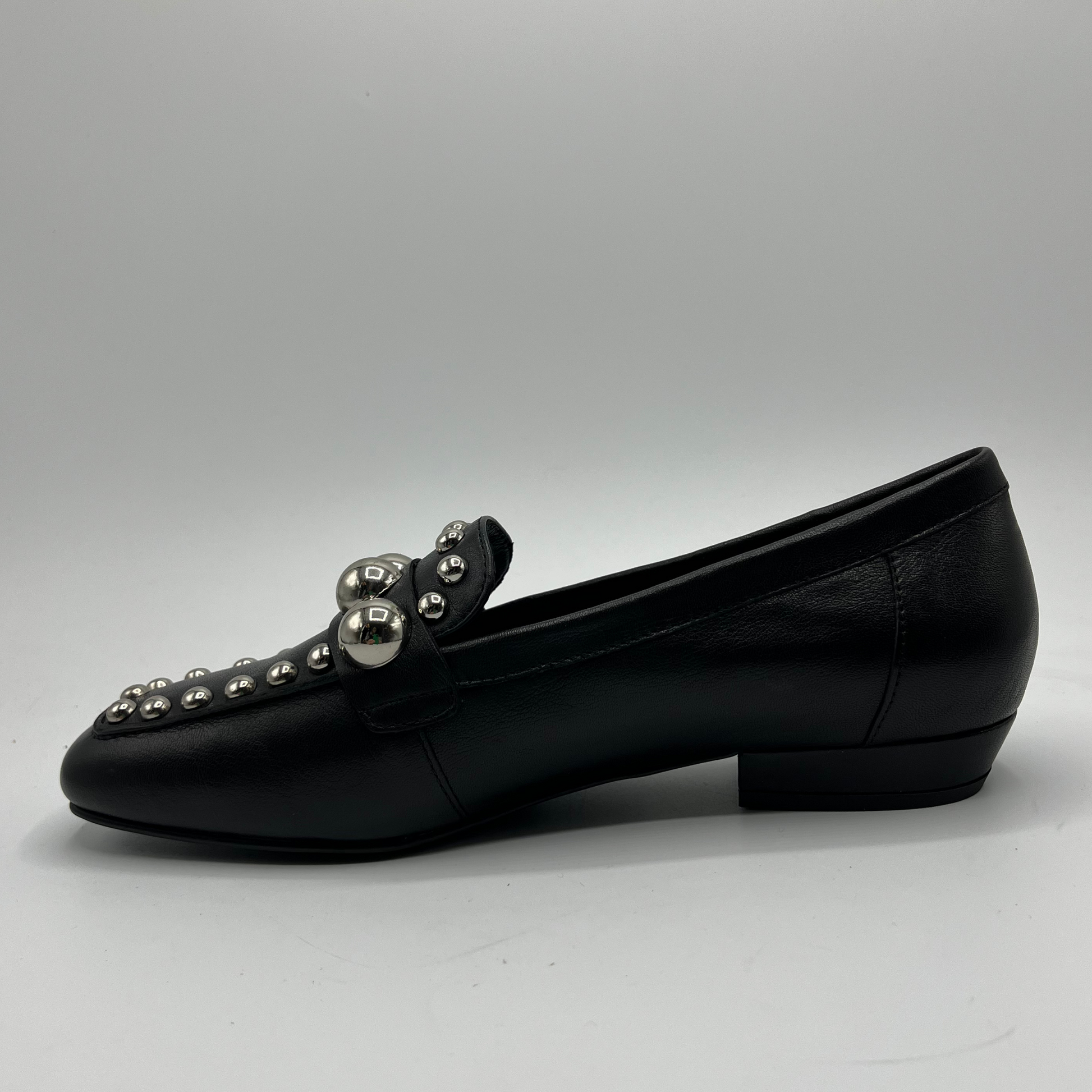 Black loafer shoe with silver embellishments on a gray background