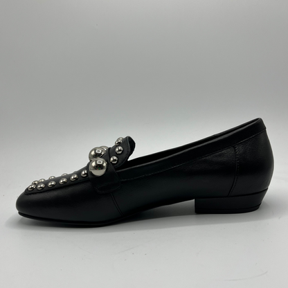 Black loafer shoe with silver embellishments on a gray background
