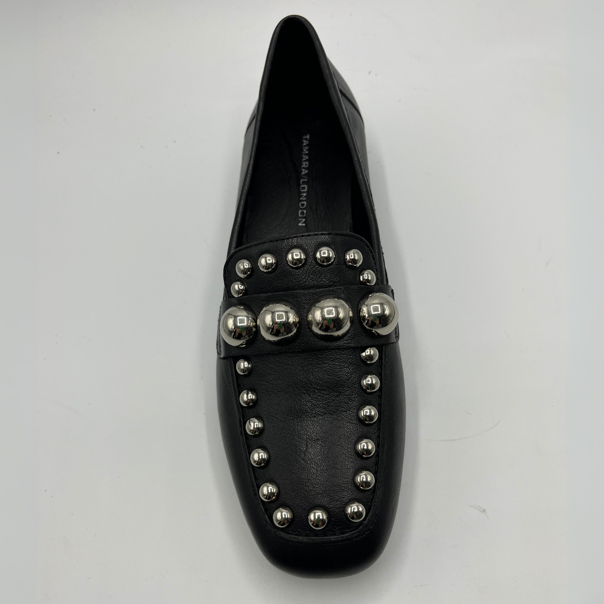 Black loafer shoe with silver studs on a light gray background