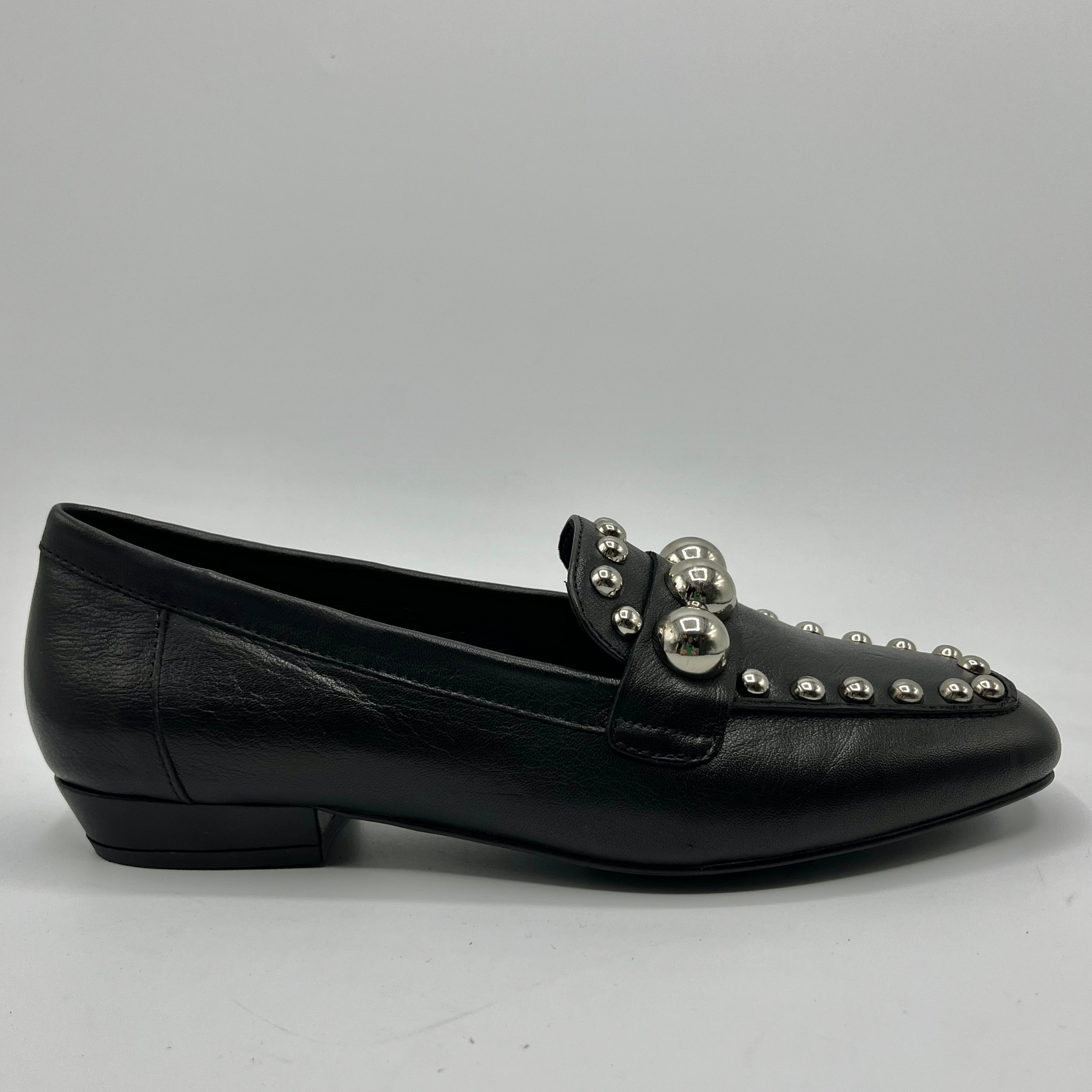 Black loafer shoe with silver embellishments on a gray background