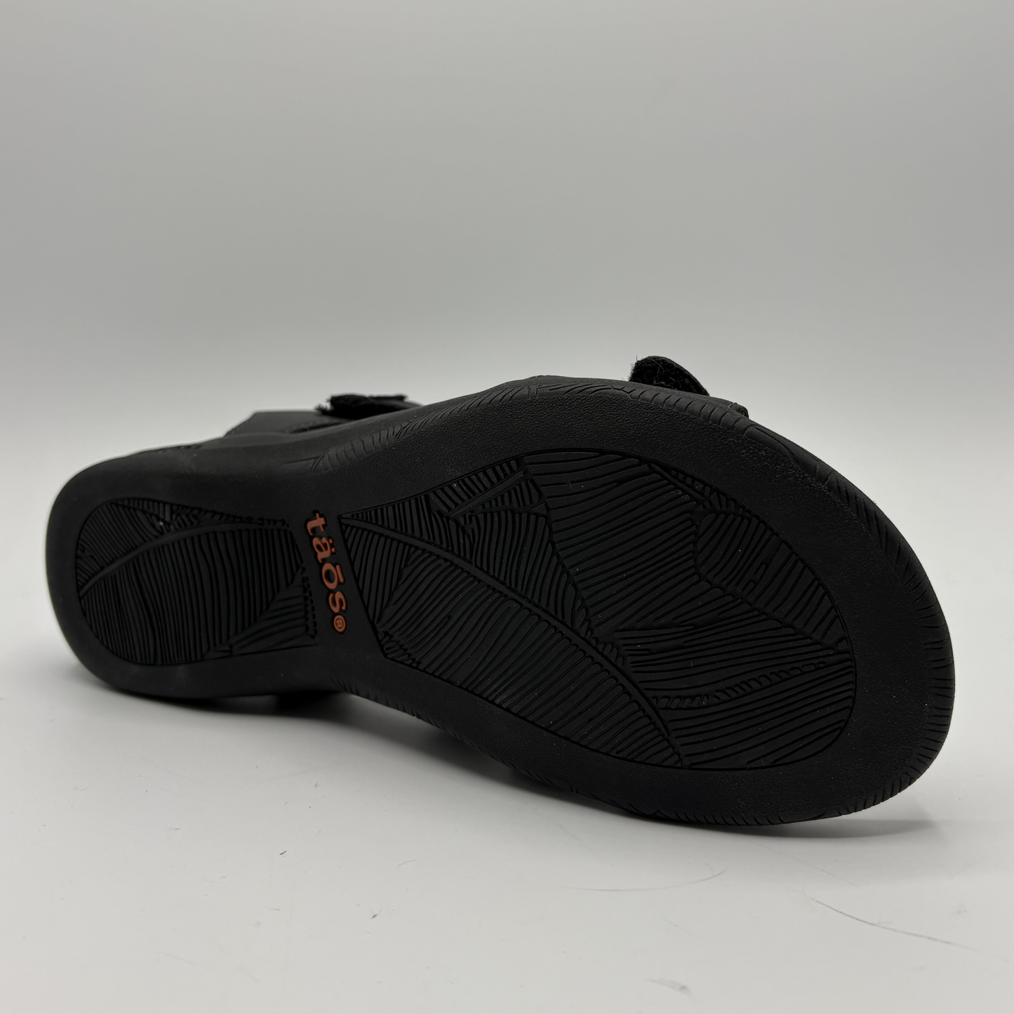 Black sandal with 'Taos' branding on a white background