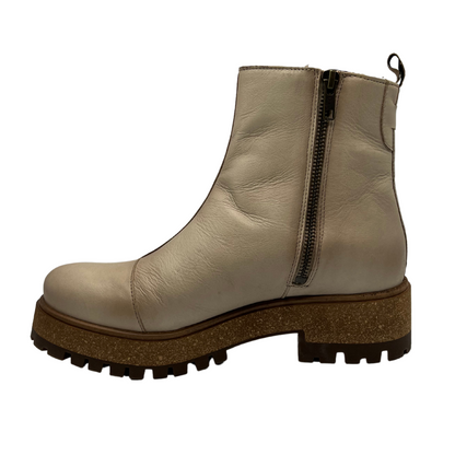 Left facing view of ivory leather short boot with rubber and cork outsole with inner zipper closure and pull on tab