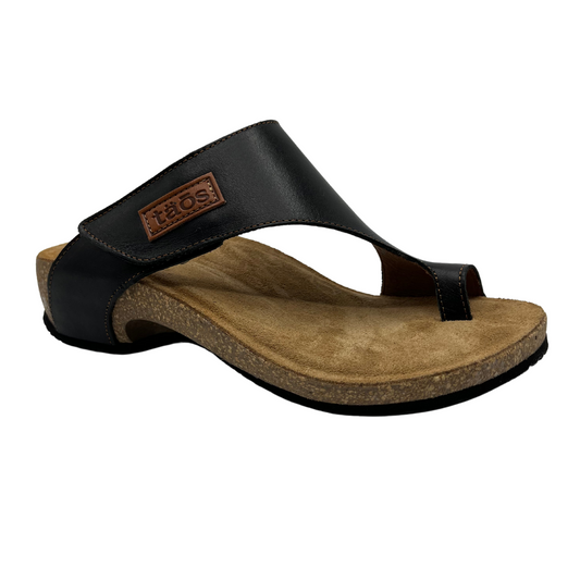 45 degree angled view of black leather sandal with brown leather lined footbed. Hook and loop closure on strap and toe strap