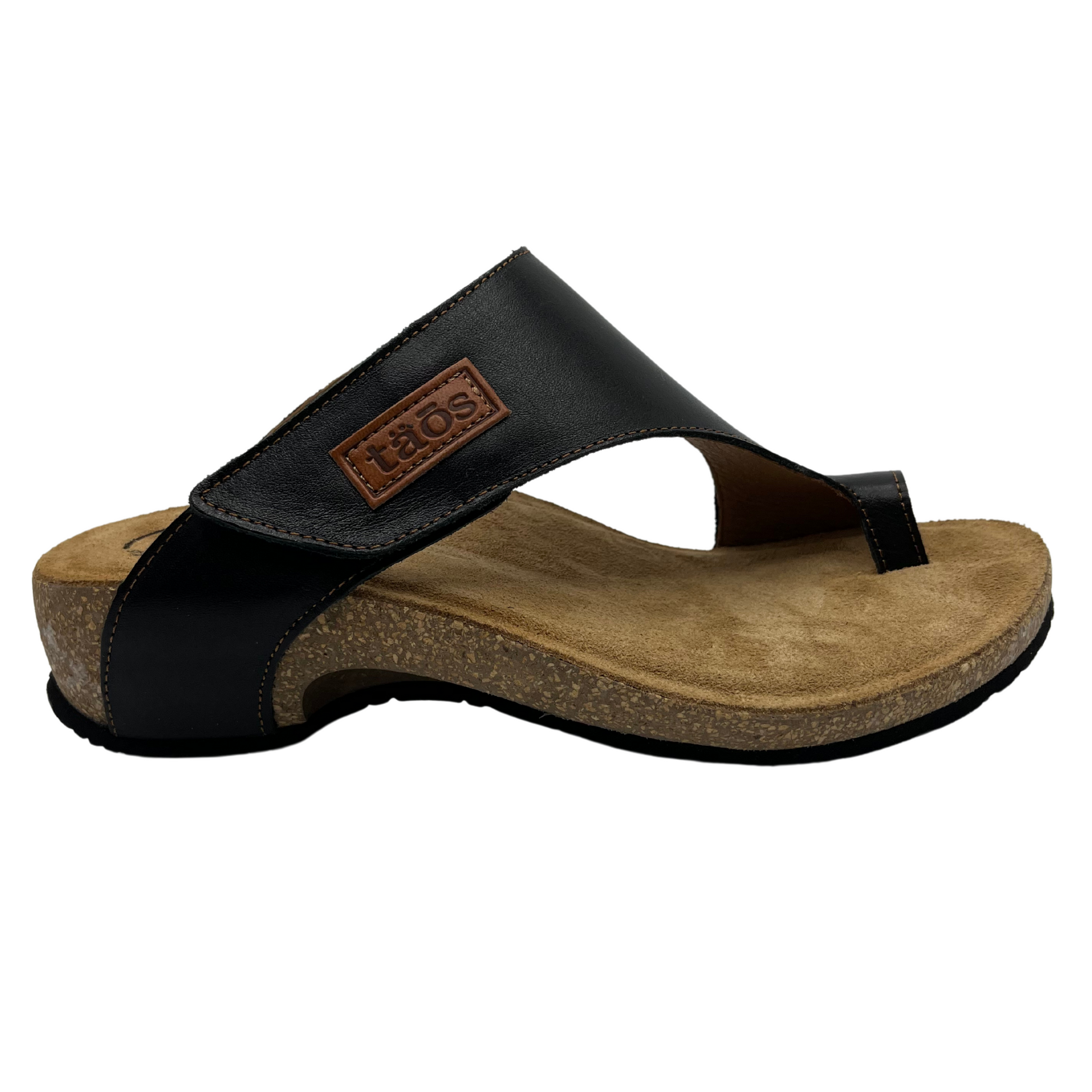Right facing view of black leather sandal with brown leather lined footbed. Hook and loop closure on strap and toe strap