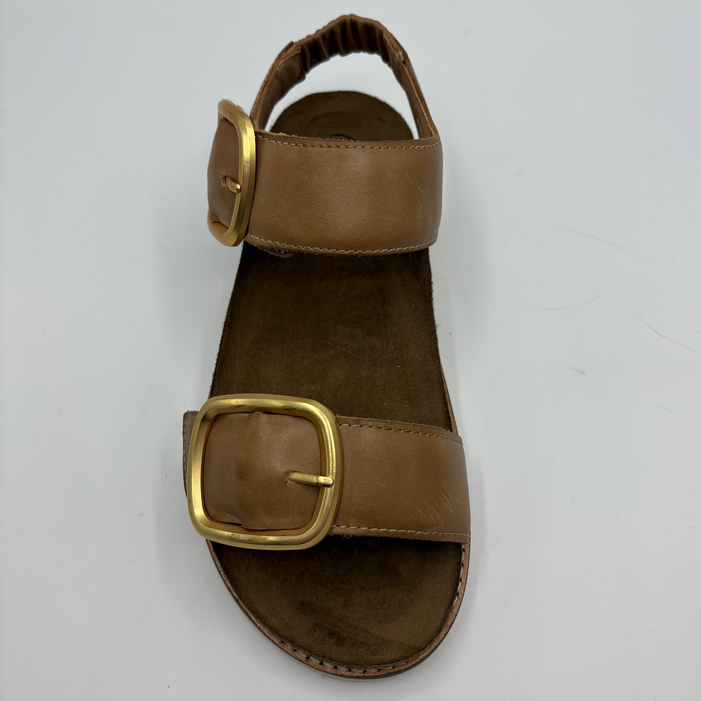 Brown sandal with gold buckle on a light gray background