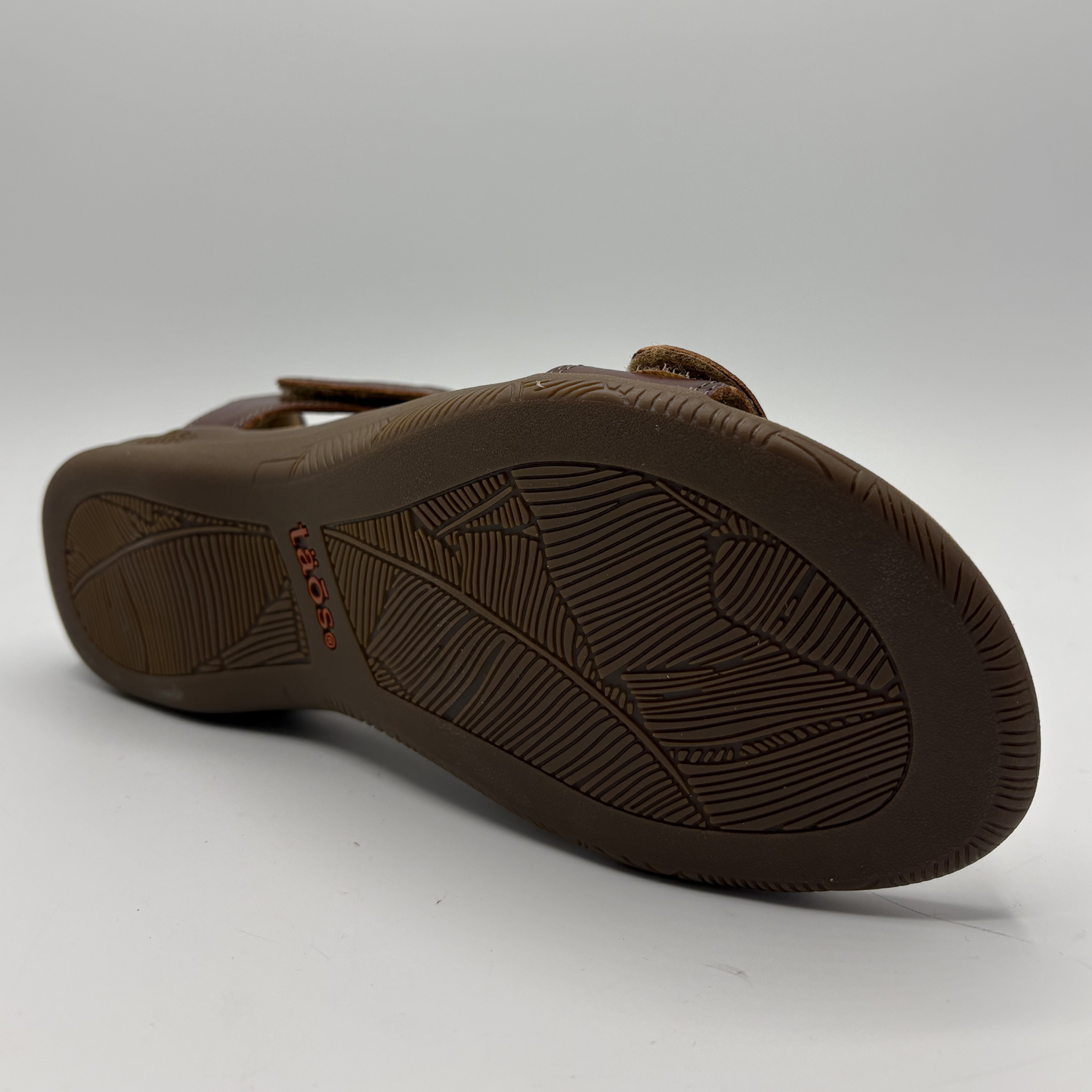 Brown sandal with textured sole on a light gray background