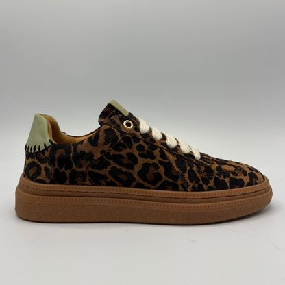 A low-top sneaker featuring a brown and black leopard print upper, white laces, a tan rubber sole, and a light olive green heel tab, shown against a neutral gray background.