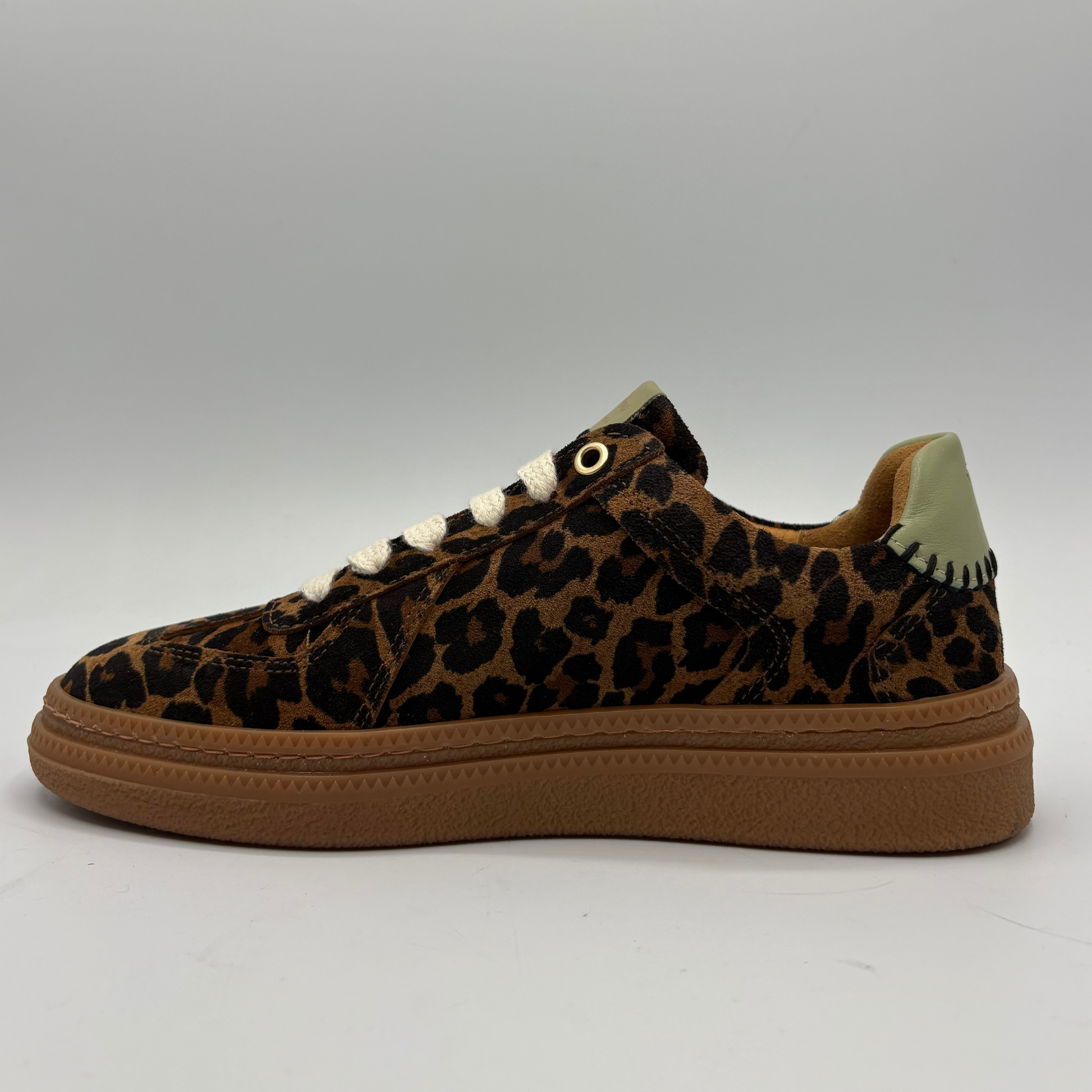 A low-top sneaker featuring a brown and black leopard print upper, white laces, and a thick brown gum sole, shown from a side profile view against a neutral gray background.