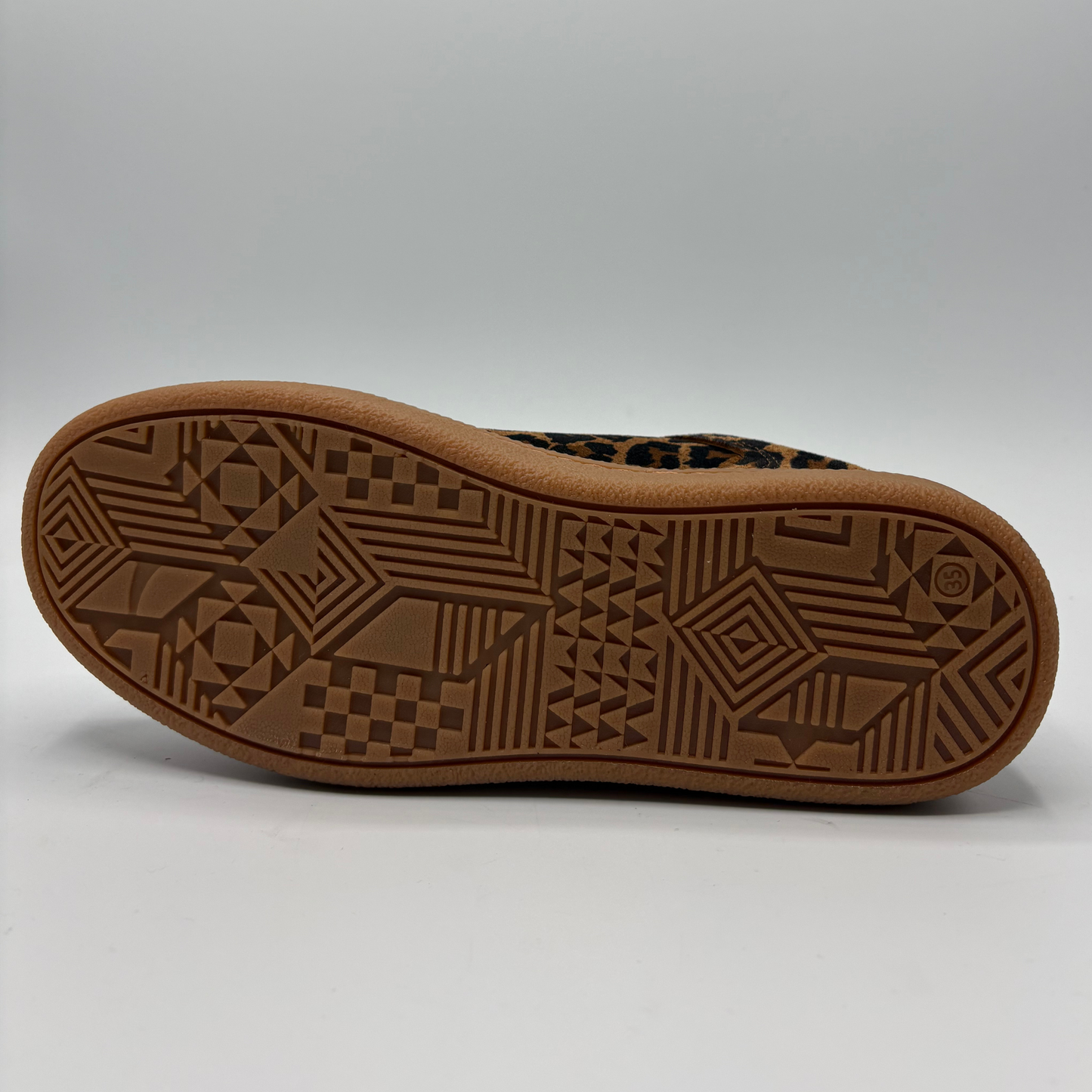 The outsole of a brown shoe with a geometric tread pattern, shown against a neutral gray background.
