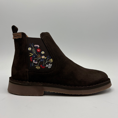 A dark brown suede Chelsea boot with colorful floral embroidery on the side, set against a neutral gray background.