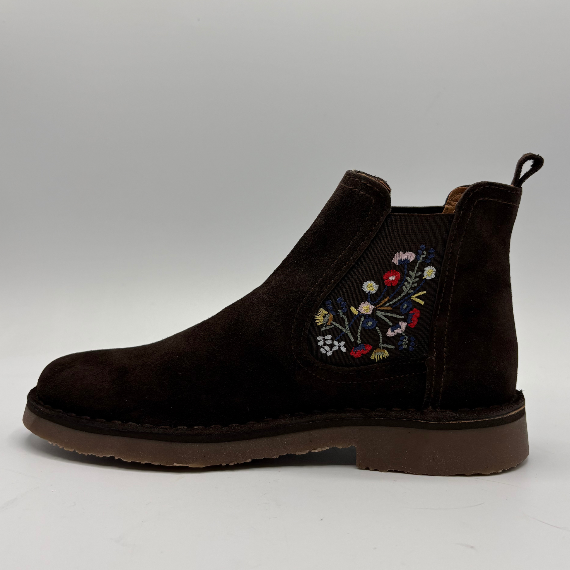 A dark brown suede Chelsea boot with colorful floral embroidery on the side, shown in profile against a neutral gray background.