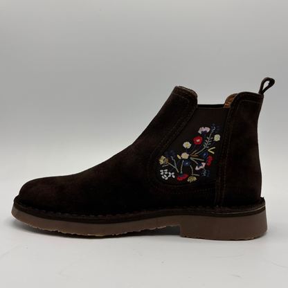 A dark brown suede Chelsea boot with colorful floral embroidery on the side, shown in profile against a neutral gray background.