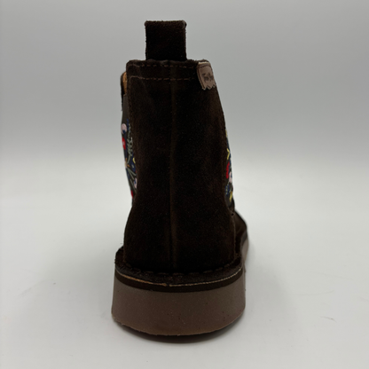 A dark brown suede ankle boot shown from the back, featuring colorful embroidered details on the side and a thick brown sole, set against a neutral gray background.