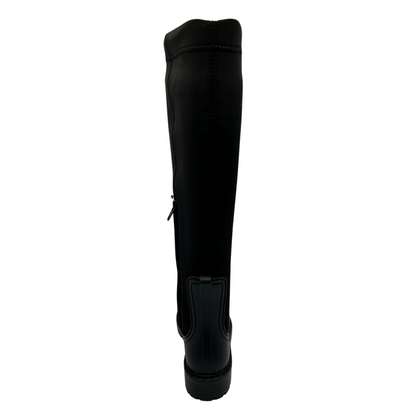 Back view of black rubber and lycra tall boot with rounded toe and black rubber outsole. Side zipper closure and pull on tab.