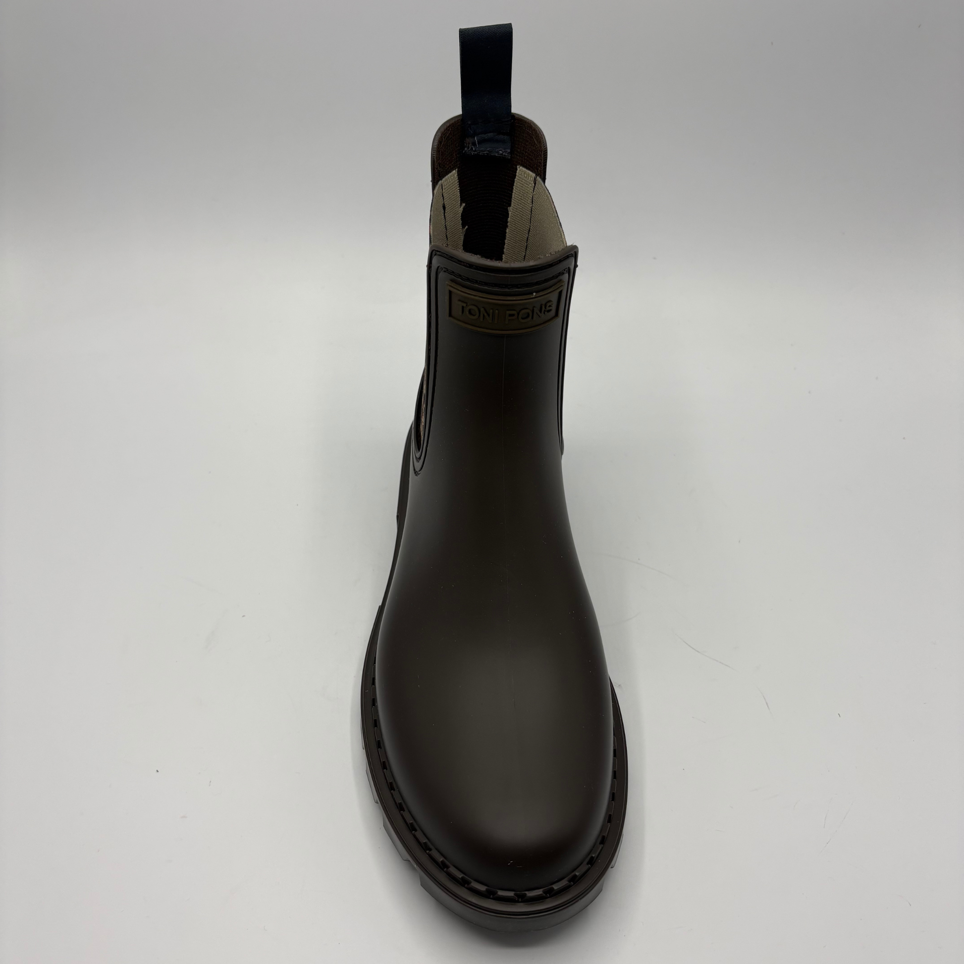 A single dark brown Chelsea rain boot with elastic side gore, a pull tab, photographed against a neutral light gray background.