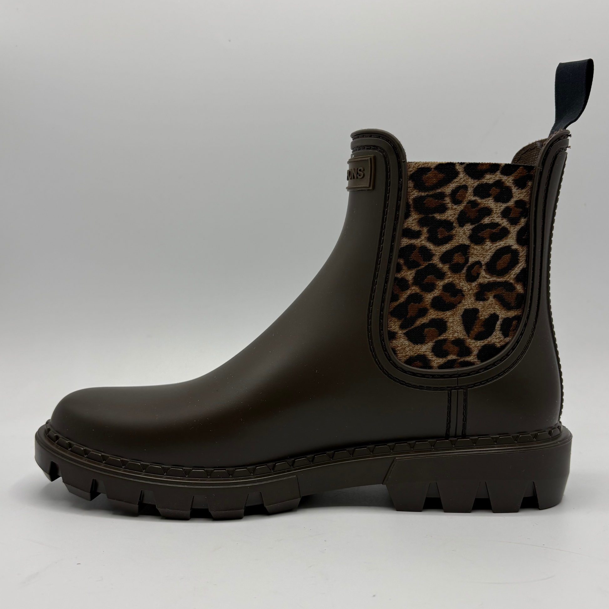 A dark brown rubber rain boot with a leopard print elastic side panel, shown in profile against a light gray background.