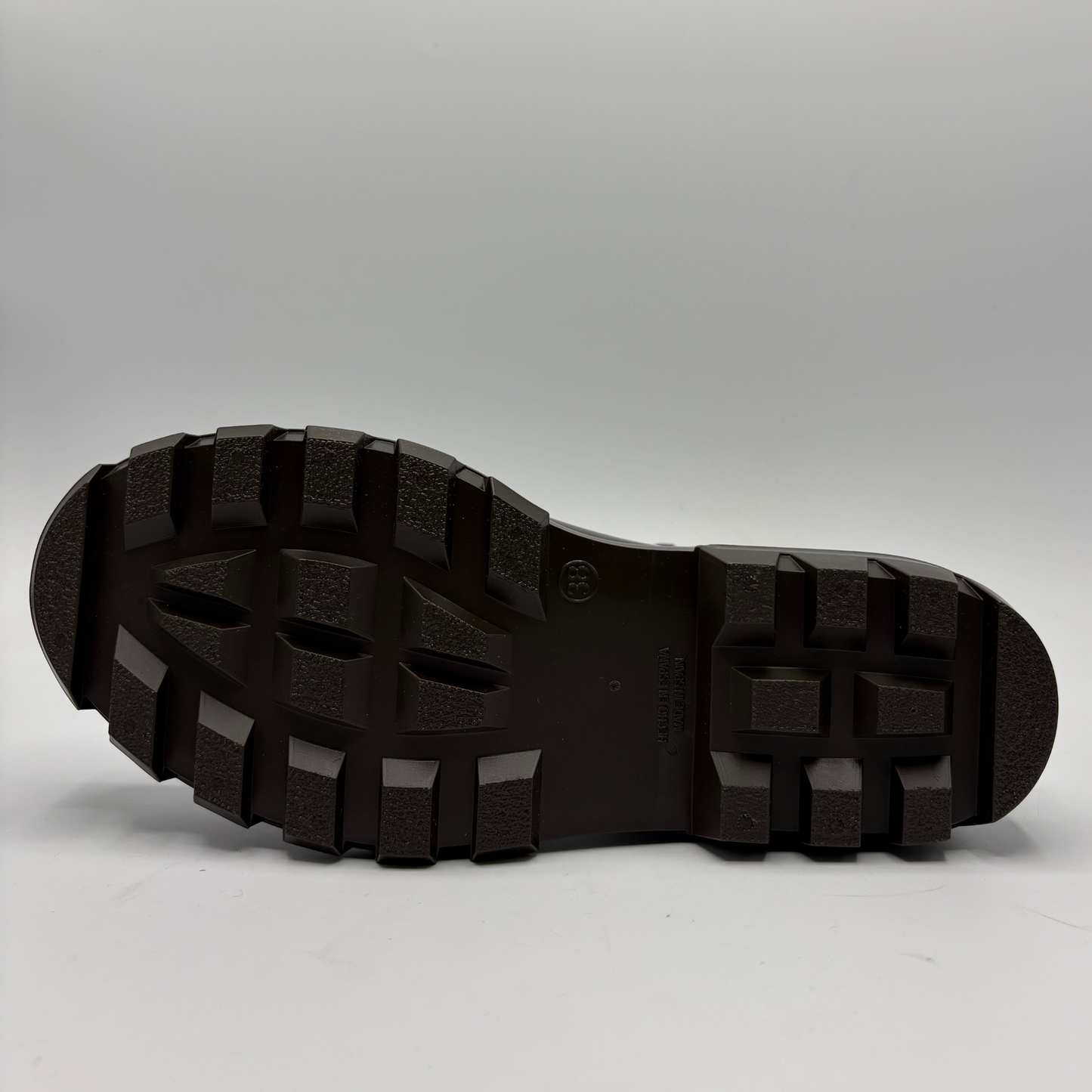 The treaded black rubber outsole of a heavy-duty boot, shown from a bottom-up perspective against a neutral gray studio background.
