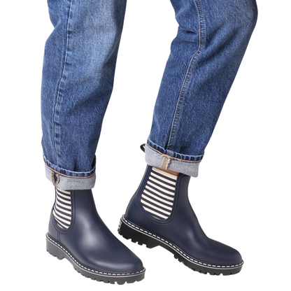 View of a pair of short navy rain boots with elastic side gores being modelled by a person wearing blue jeans