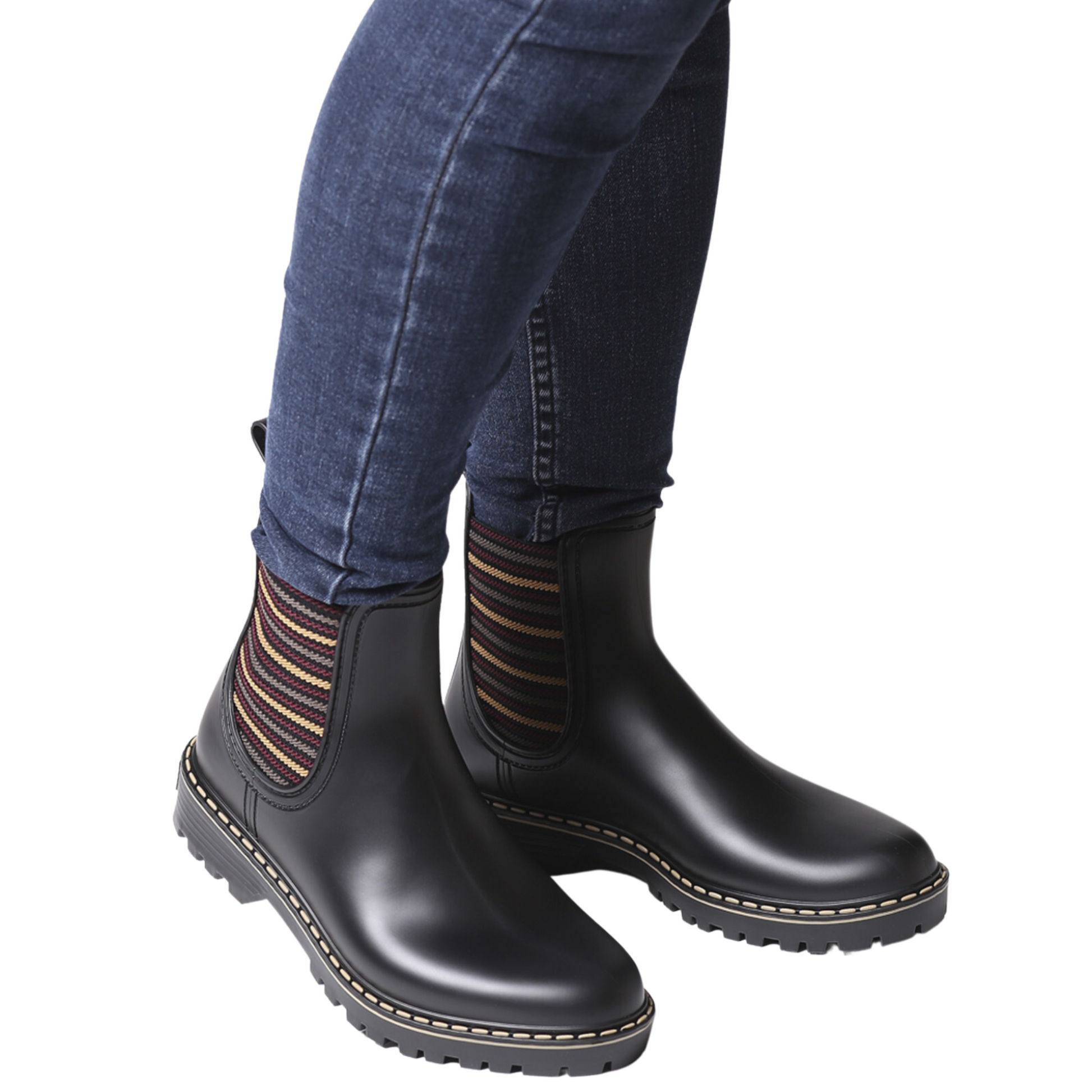 View of a pair of short black rain boots with striped elastic side gores being modelled by a person wearing jeans