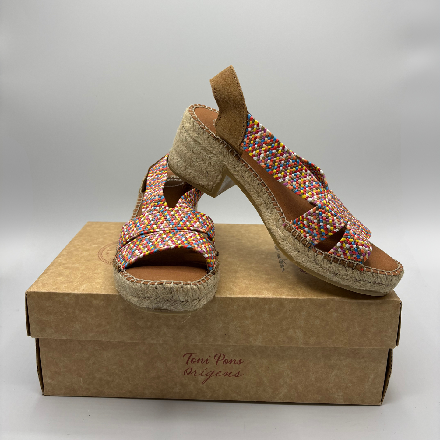 Colourful woven sandals on a brown shoe box with 'Toni Pons Origins' branding.