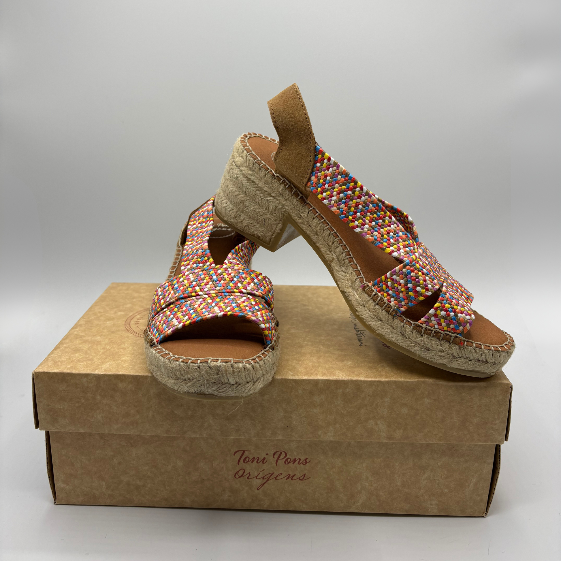 Colourful woven sandals on a brown shoe box with 'Toni Pons Origins' branding.