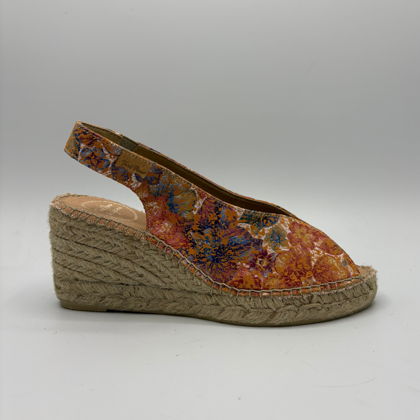 Wedge sandal with floral patterned upper and jute sole on a gray background