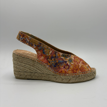 Wedge sandal with floral patterned upper and jute sole on a gray background