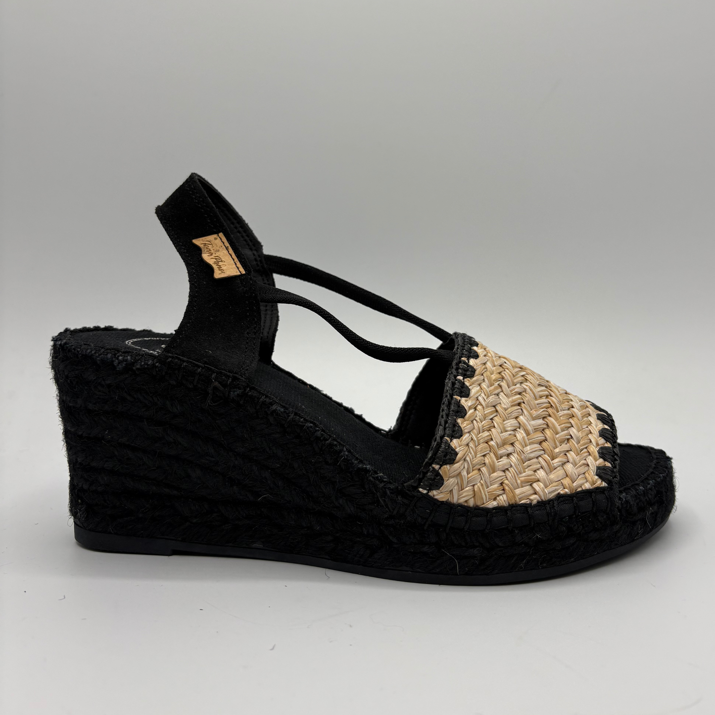 Black wedge sandal with woven design on a gray background