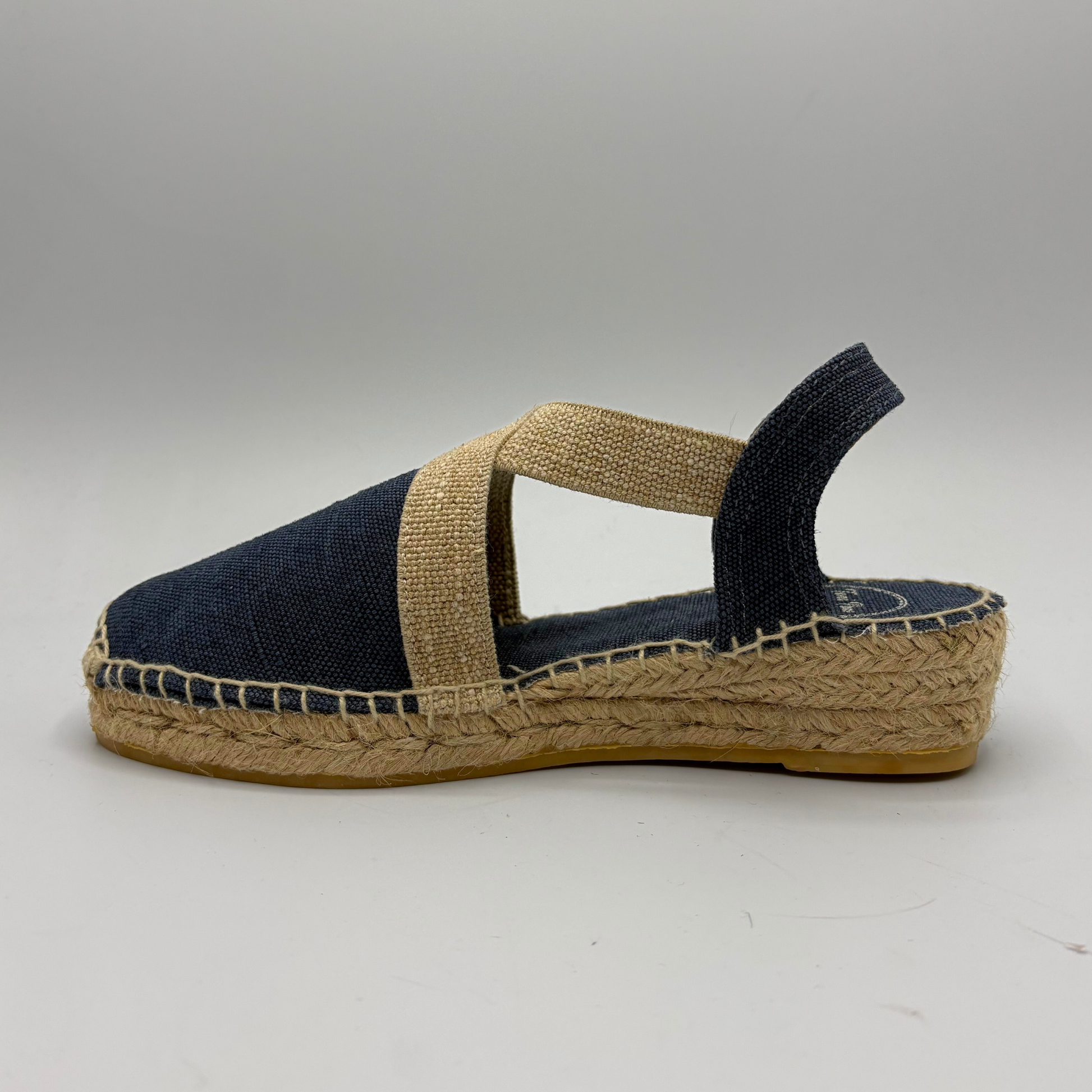 Navy blue espadrille sandal with a brown sole on a gray background