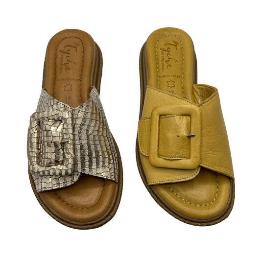 Top view of two leather slip on sandals side by side. One is gold with a snake print design and the other one is yellow. Both have a leather lined, cushioned footbed and open toe