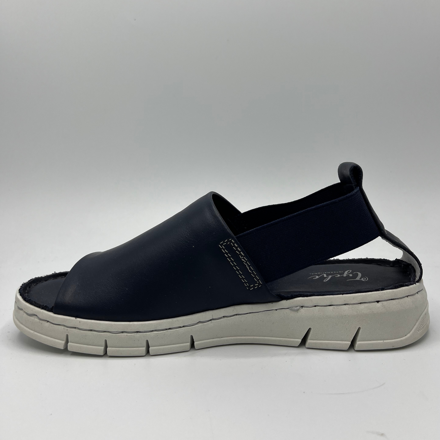 Left facing view of a slip on shoe with elasticated side bands, peep toe and a white rubber outsole.