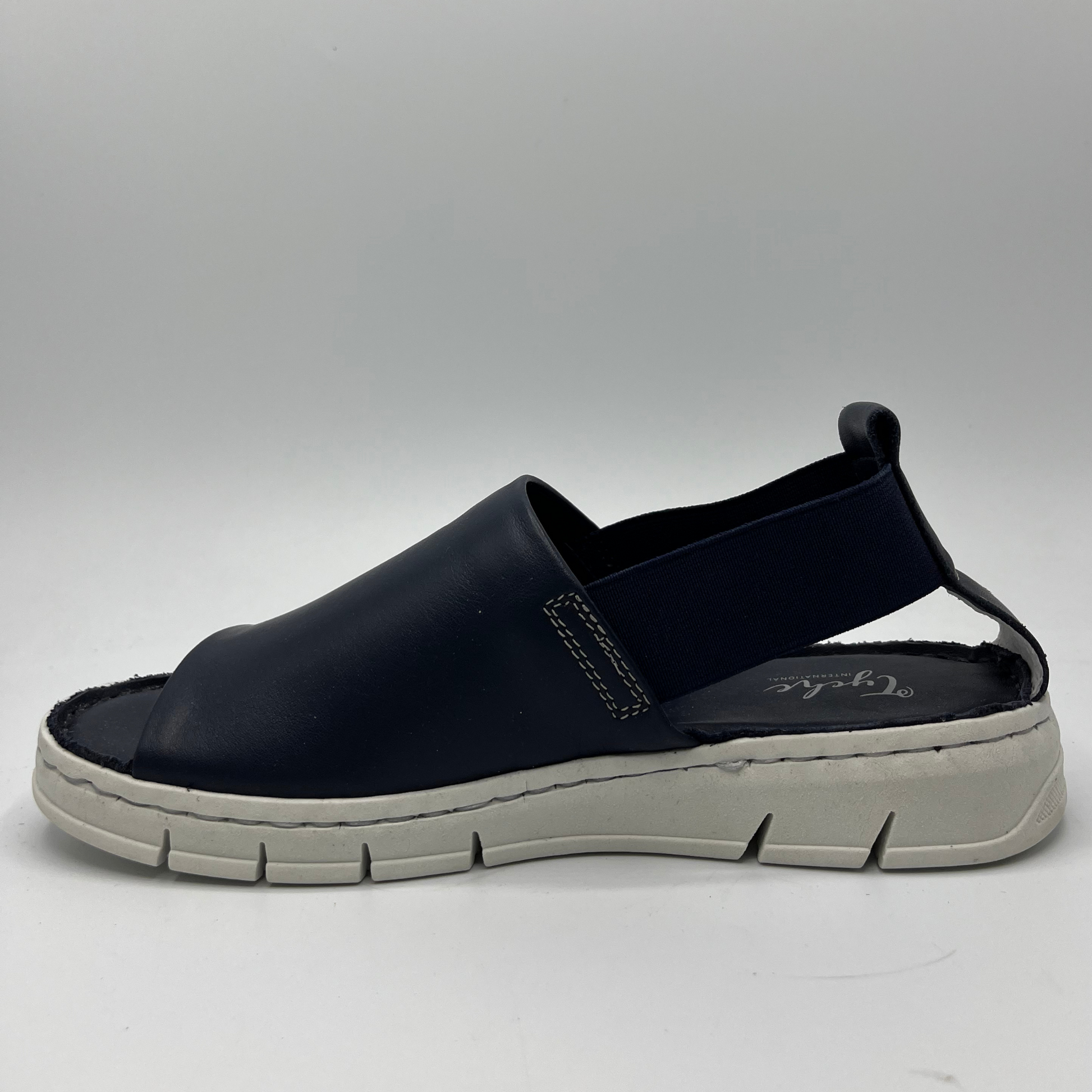 Left facing view of a slip on shoe with elasticated side bands, peep toe and a white rubber outsole.