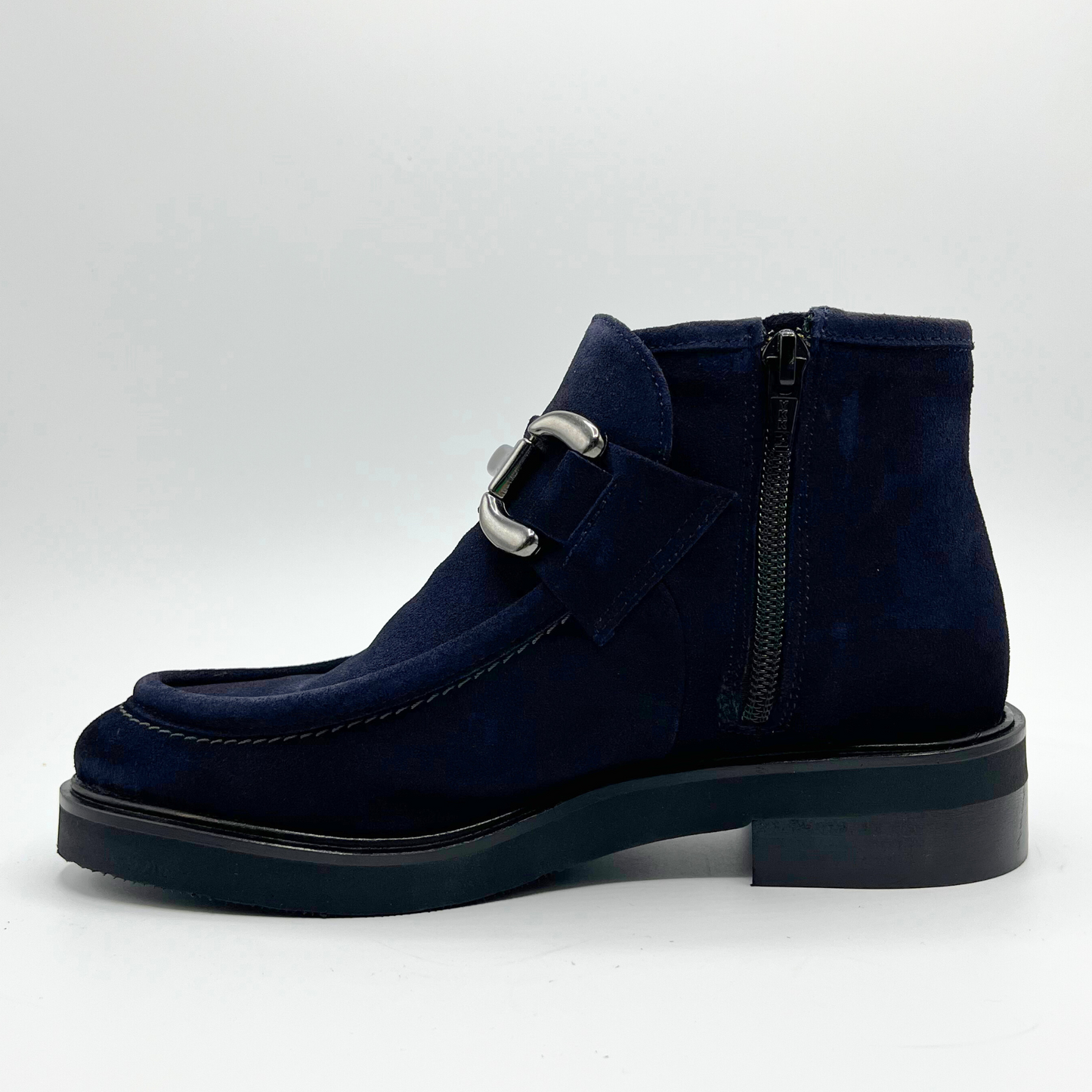 Navy blue suede boot with a silver buckle on a light gray background