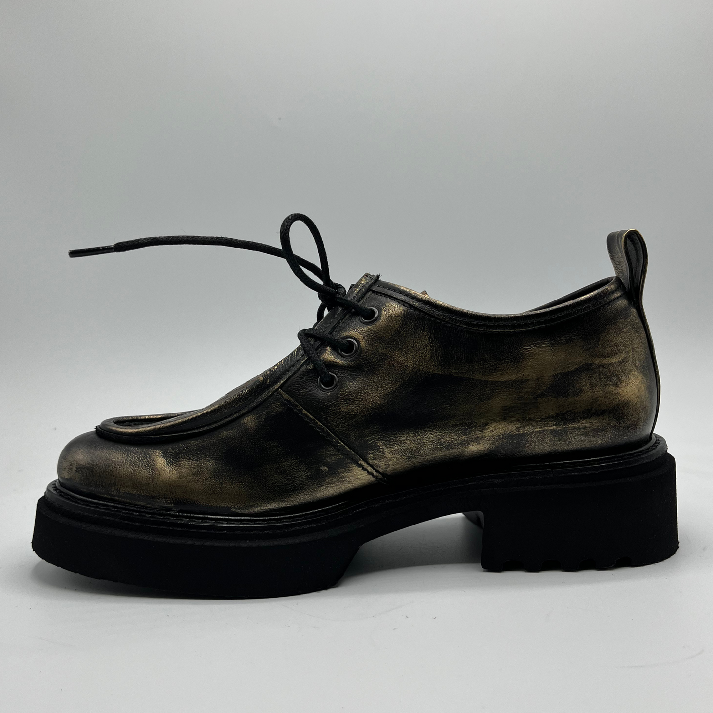 Gold leather shoe with thick sole on a light gray background