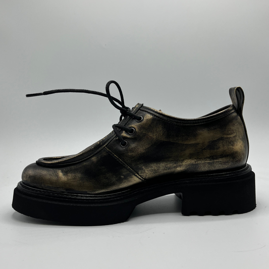 Gold leather shoe with thick sole on a light gray background
