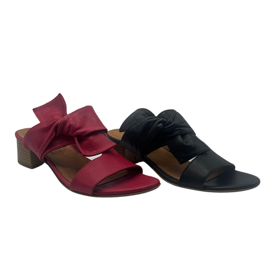 45 degree angled view of a pair of leather sandals. One is fuchsia pink leather and the other is black leather. Both have a block heel, peep toe and knot detail.