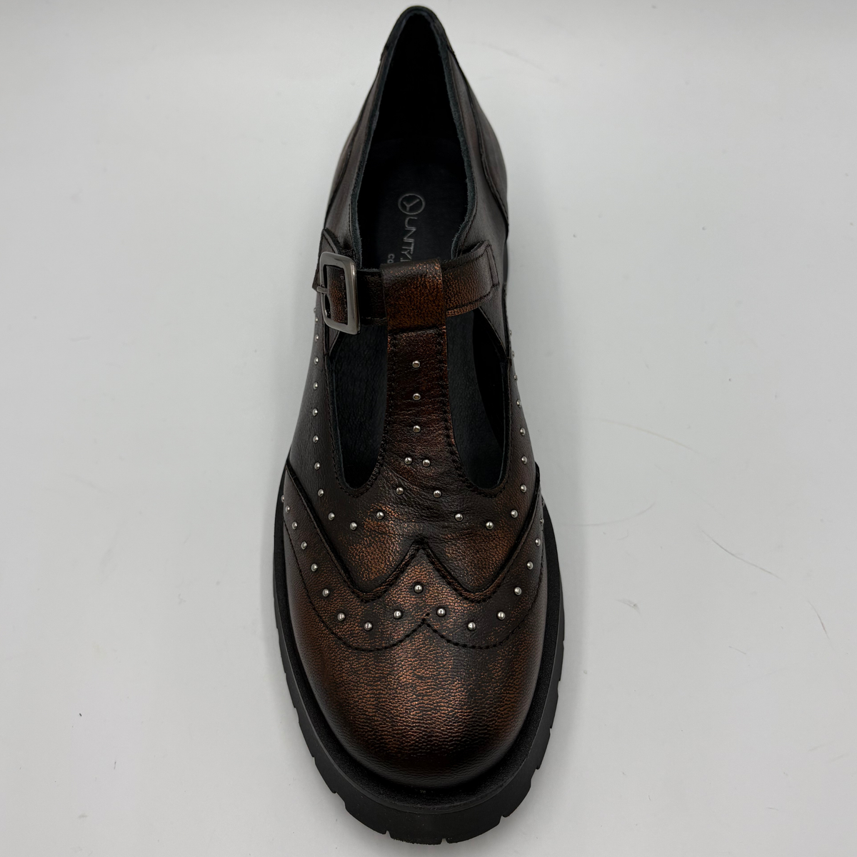 A single brown distressed leather T-strap Mary Jane shoe with silver stud detailing and a black chunky lug sole, shown from the top view on a light gray background.