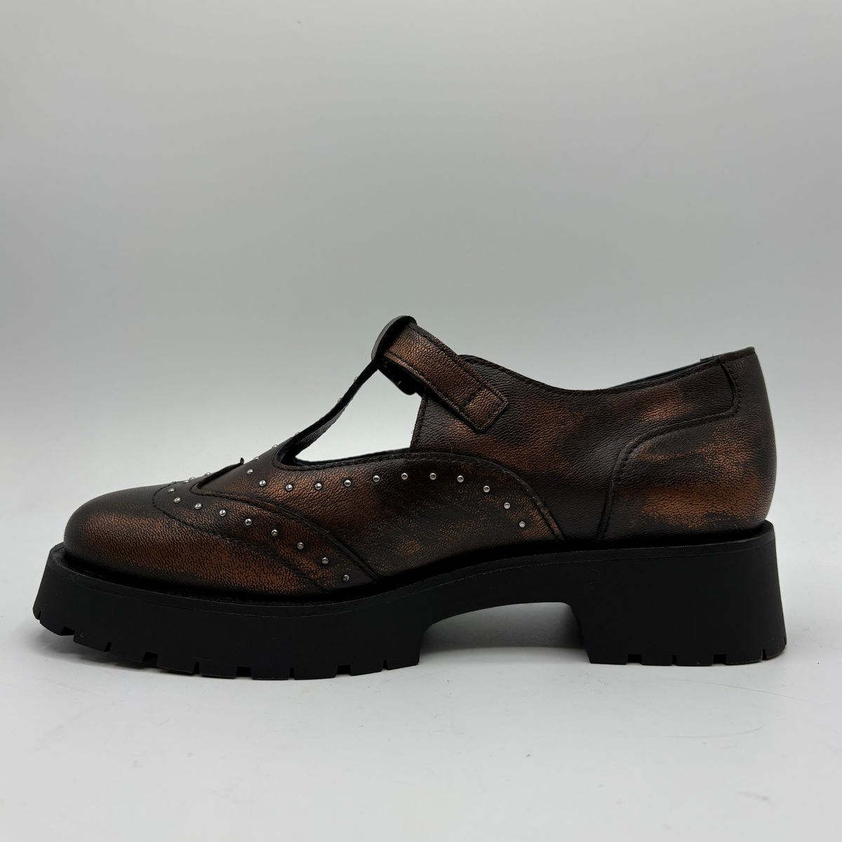 A single brown distressed leather T-strap Mary Jane shoe with silver stud detailing and a black chunky lug sole, shown from a side profile on a light gray background.